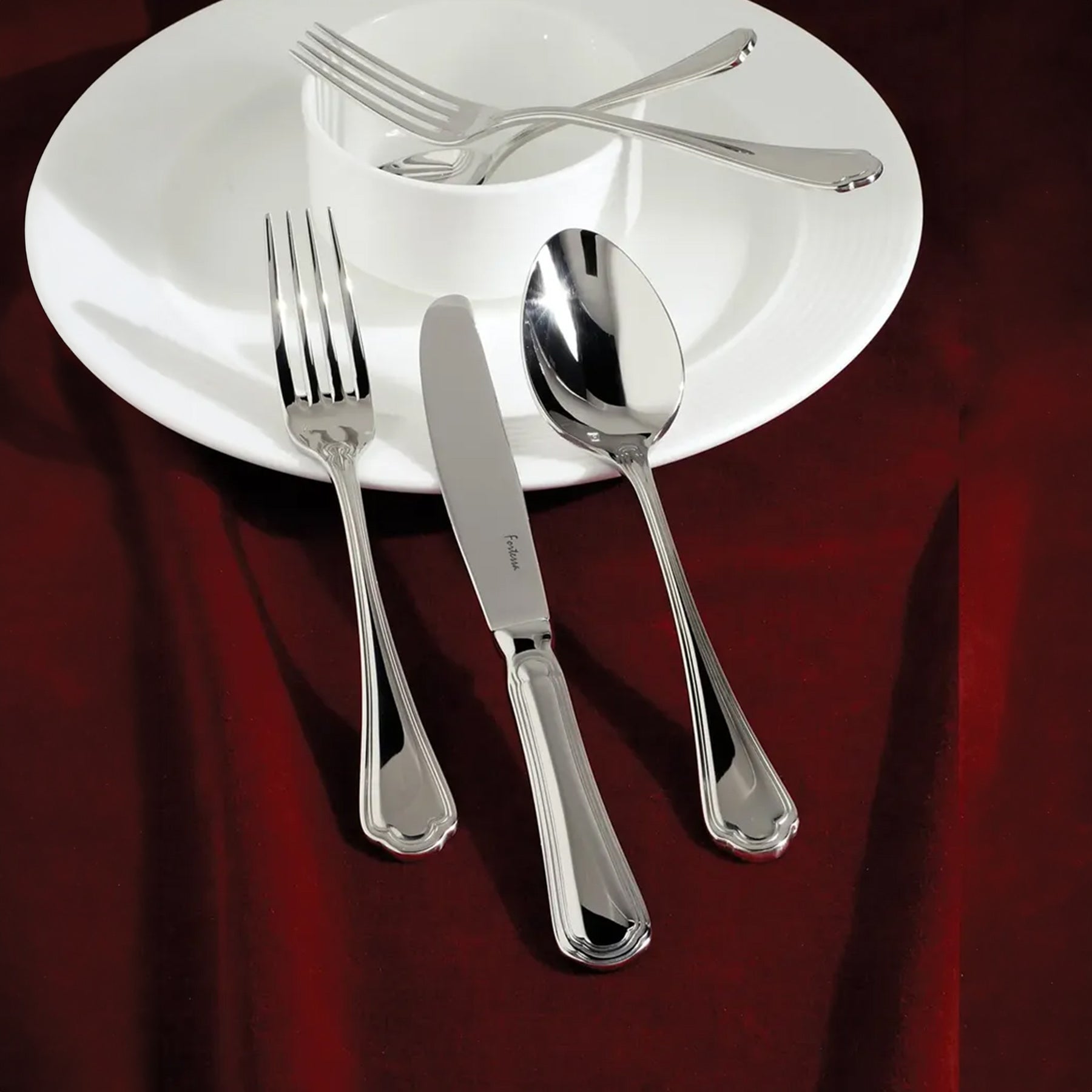 Set de cubiertos de gala de la colección Medici de Fortessa con detalles grabados sobre un mantel de damasco.
