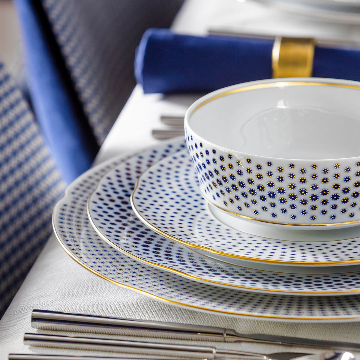 Vajilla de lujo en porcelana blanca con bordes dorados sobre una mesa de marmol.