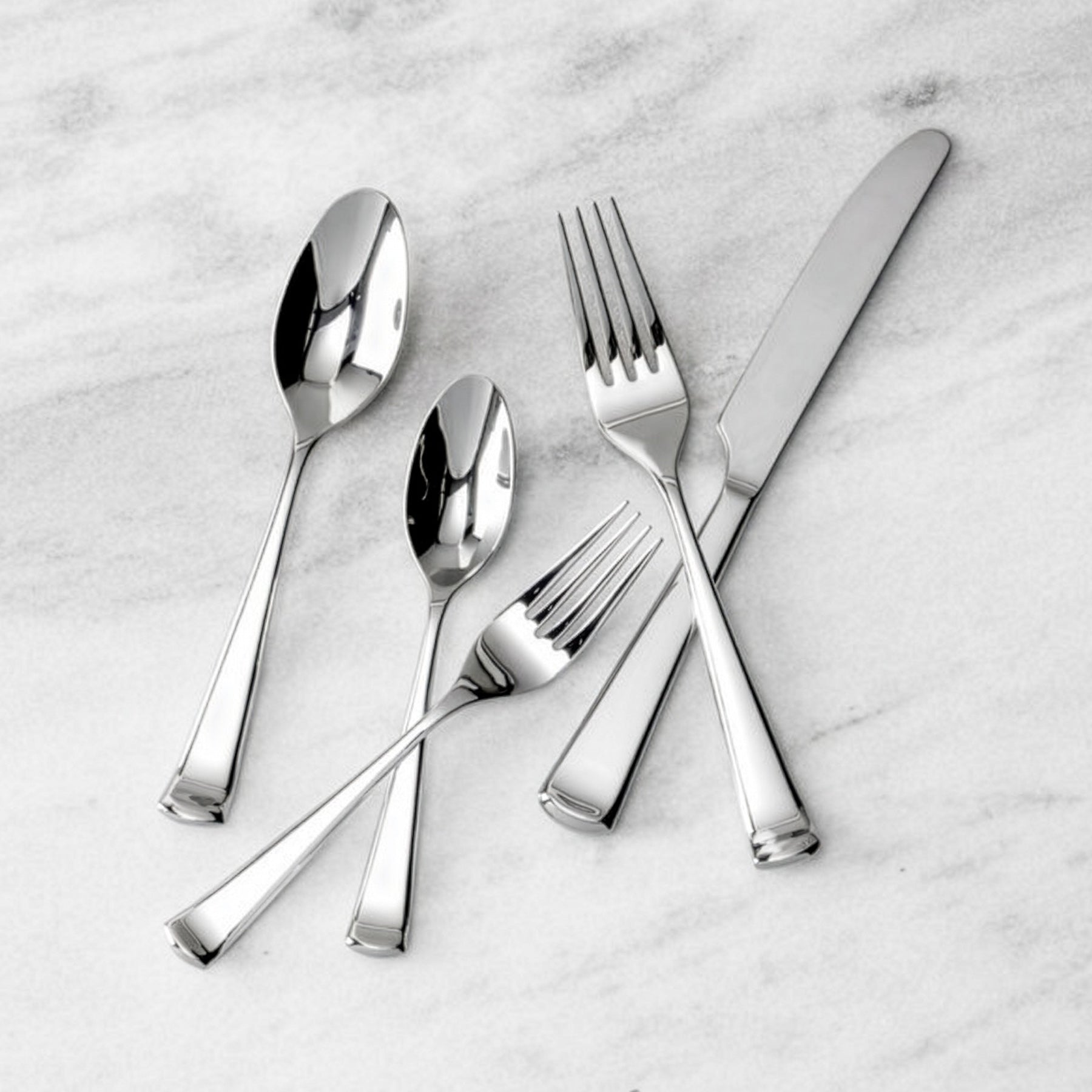 Set de cubiertos premium de la colección Honor de Fortessa de diseño contemporáneo y pulido espejo sobre una mesa de marmol.