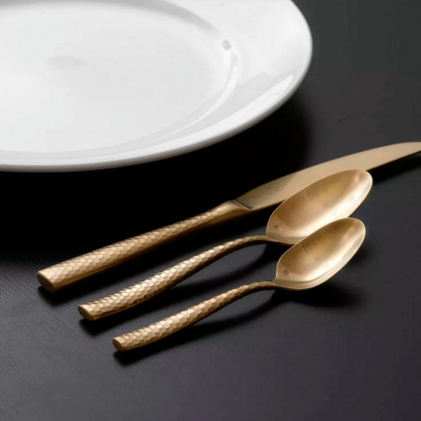 Set de cubiertos de gran gala de la colección Lucca Faceted Gold de Fortessa con acabado en oro pulido espejo sobre una mesa oscura.