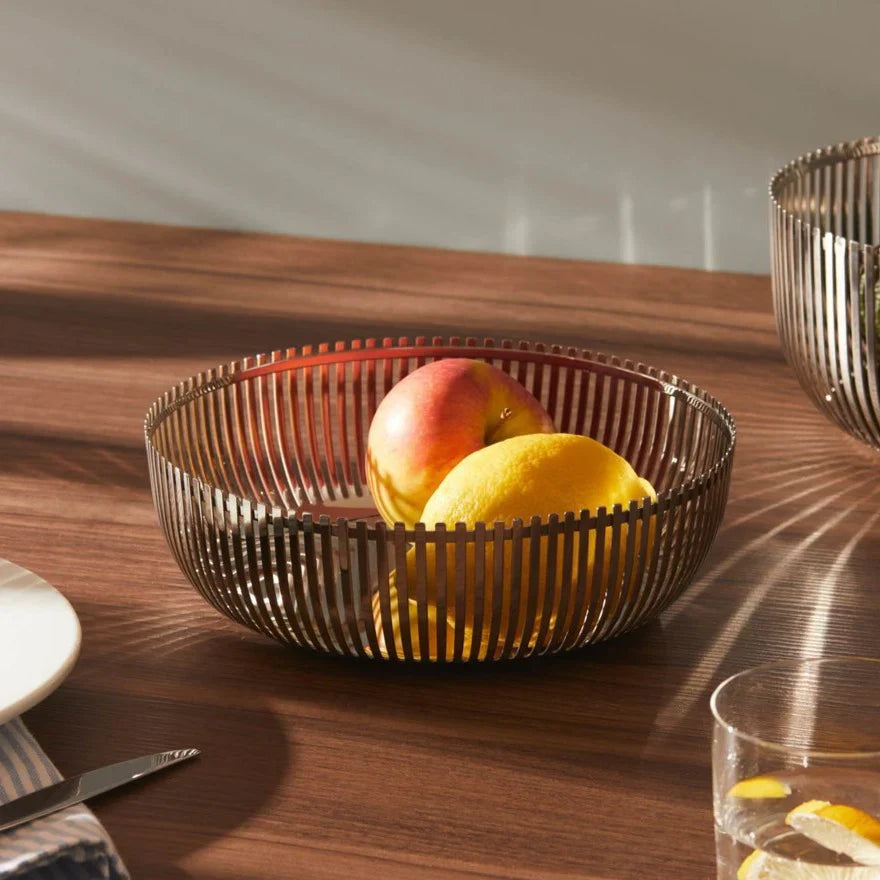 Frutero de metal con un diseño de rejilla, lleno de frutas de colores vibrantes.