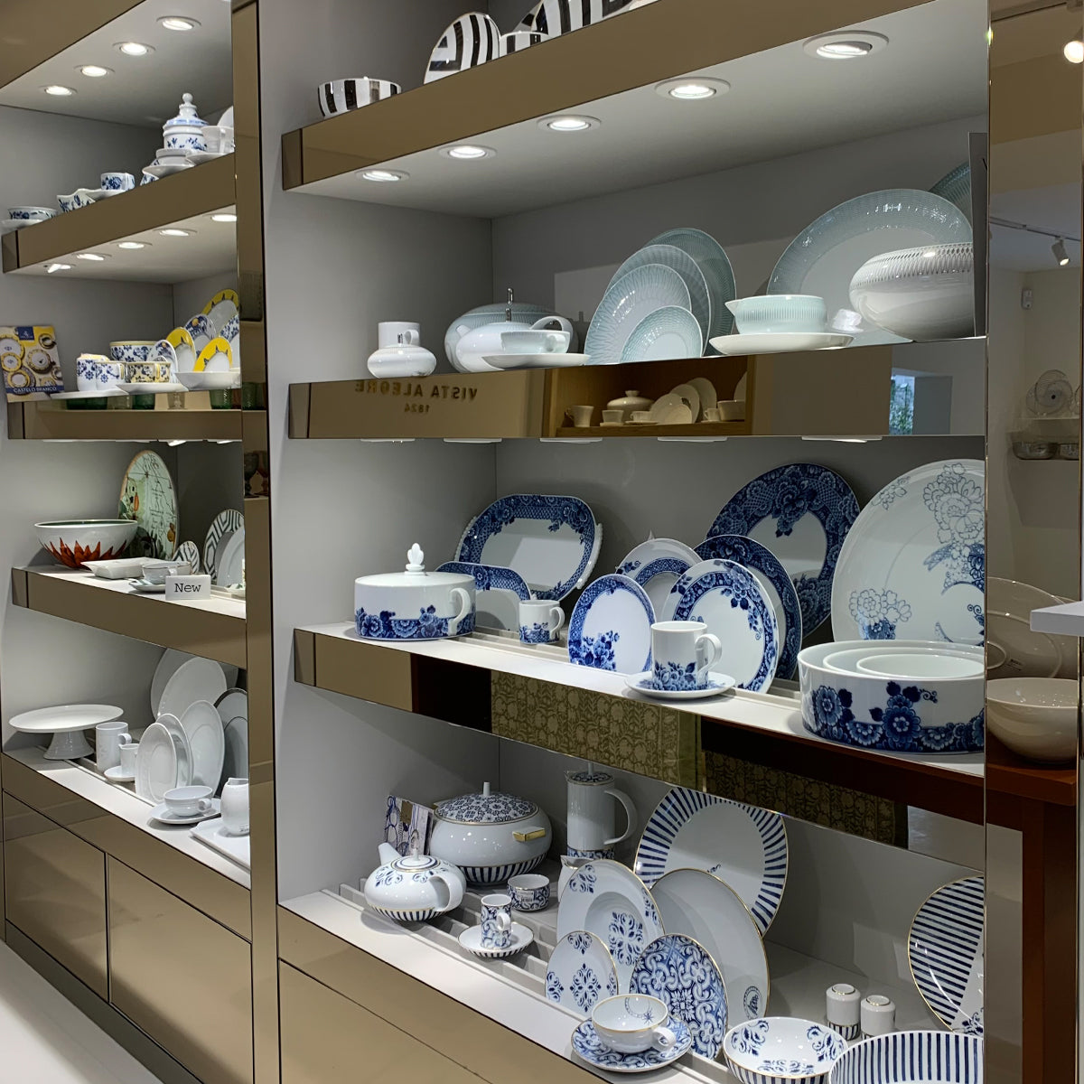 Mueble con vajillas de porcelana blanca, con bordes dorados y plateados de nuestras colecciónes de lujo.